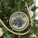 A circular ornament with a lionfish design is hanging on a Christmas tree, surrounded by other ornaments and lights.