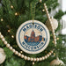 A circular ornament on a Christmas tree, featuring the text "MADISON, WISCONSIN, USA" and an illustration of the Madison, Wisconsin state capitol building.
