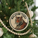 A round ornament on a Christmas tree featuring a tiger's face, with the text "MALAYAN TIGER" around the image.