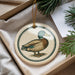A decorative ornament featuring a duck is displayed in a box, surrounded by pine branches.