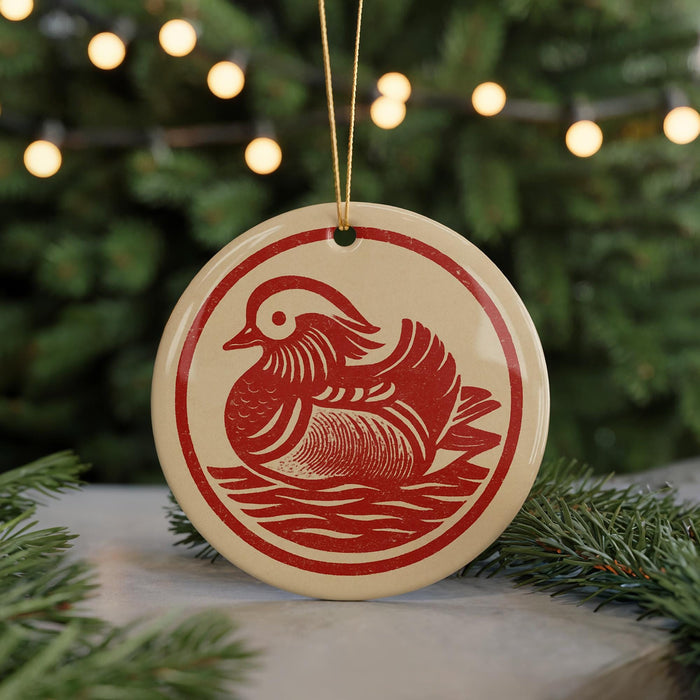 A red and white ceramic ornament featuring a duck design, hanging from a string and placed on a surface with pine branches in the background.