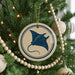 A Christmas tree decorated with ornaments, including a circular ornament with a blue stingray design and a string of wooden beads.
