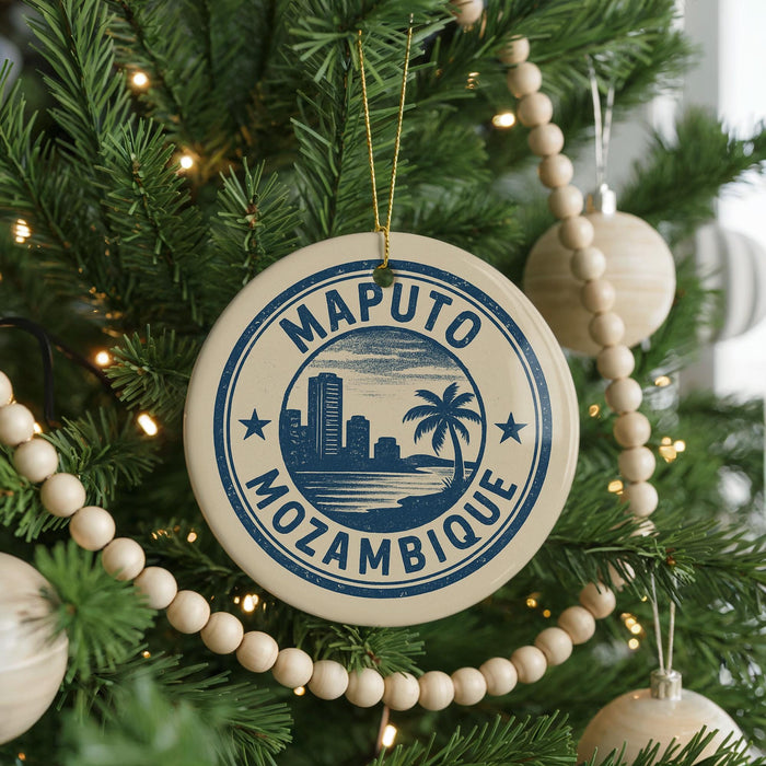 A circular ornament on a Christmas tree with the text "MOPUTO MOZAMBIQUE" printed on it, surrounded by other ornaments and lights.