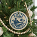 A circular ornament on a Christmas tree with the text "MOPUTO MOZAMBIQUE" printed on it, surrounded by other ornaments and lights.