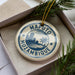 A circular ornament with the text "Mazuto Mozambique" printed on it, surrounded by a decorative border and a small palm tree image.