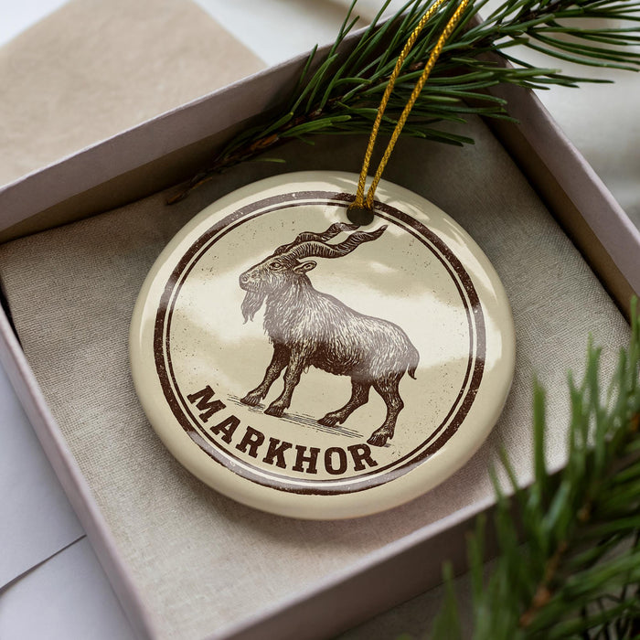 A circular ornament with a brown and white design featuring a goat, and the word "MARKHOR" written on it.