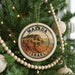 A circular ornament on a Christmas tree, featuring an illustration of Masada, the historic city of Jerusalem, with the text "MASADA ISRAEL" prominently displayed.