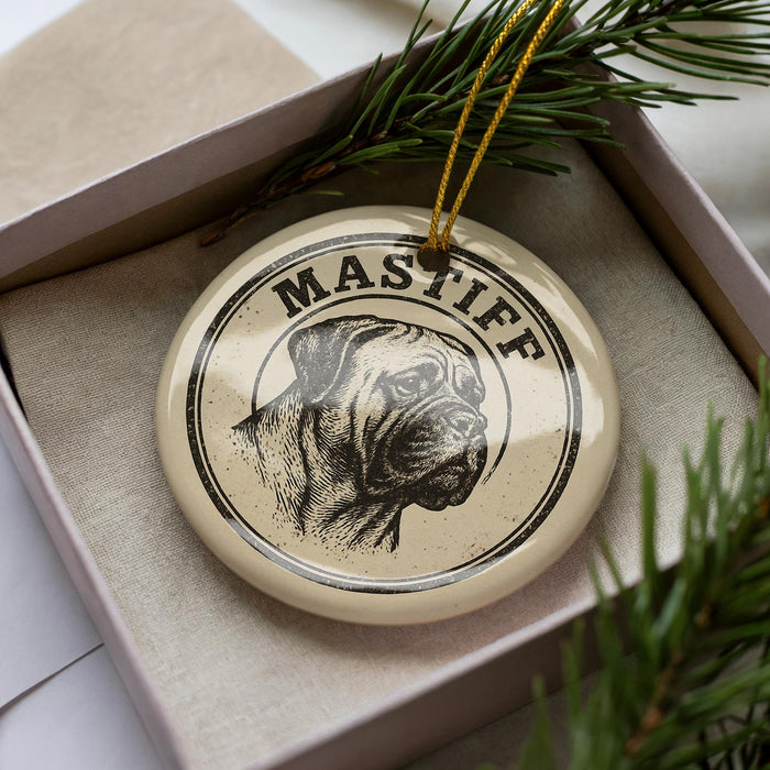 A circular ornament with a dog's head and the word "Mastiff" printed on it, placed inside a box with pine branches.