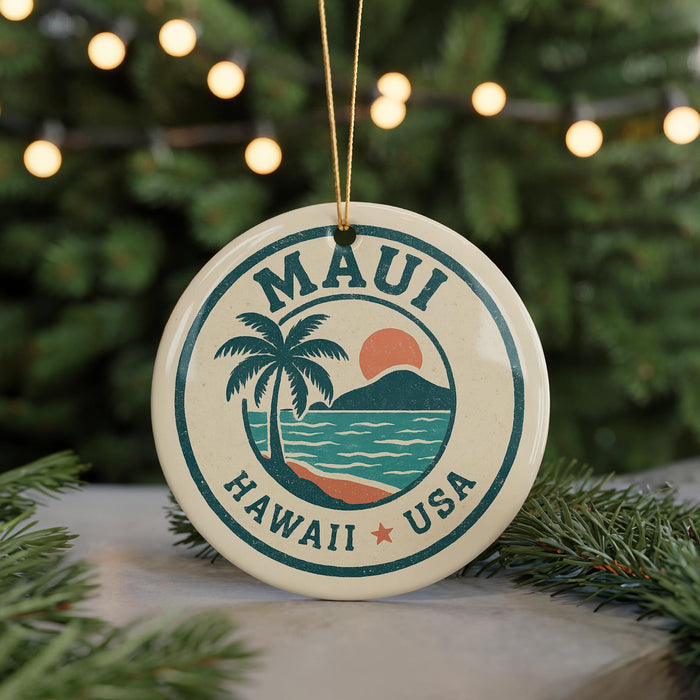A circular ornament with the text "MAUI HAWAII USA" and a palm tree design, hanging from a string against a background of Christmas lights and greenery.