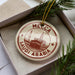 A circular ornament with the text "M Mecca Saudi Arabia" printed on it, surrounded by a decorative border.