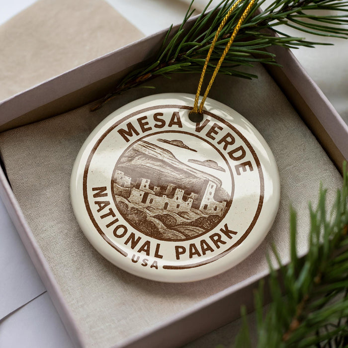 A circular ornament with the text "MESA VERDE NATIONAL PARK USA" printed on it, placed in a box with pine branches.
