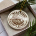 A circular ornament with the text "MESA VERDE NATIONAL PARK USA" printed on it, placed in a box with pine branches.
