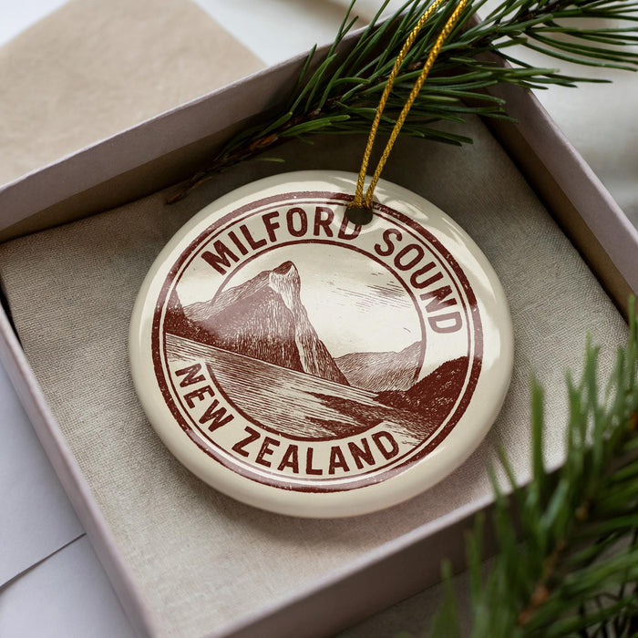 A circular ornament with the text "MILFORD SOUND NEW ZEALAND" printed on it, surrounded by pine branches.