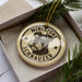 A round ornament with a dog's head and the text "MINIATURE SCHNAUZER" printed on it, placed inside a box with pine branches.