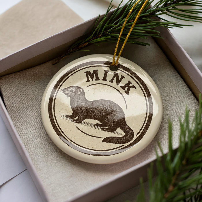 A round ornament with the word "MINK" printed on it, featuring a picture of a brown otter.