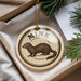 A round ornament with a mink illustration on it, placed in a box with pine branches.