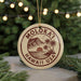 A circular ornament with the text "MOLOKA1 HAWAII USA" printed on it, surrounded by pine branches and a string of lights.