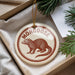 A round ornament with a brown moose illustration and the word "MONGOOSE" printed on it, hanging from a string.