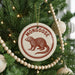 A Christmas tree decorated with ornaments, including a circular ornament with a red and white design featuring a brown moose and the word "MONGOOSE" written on it.