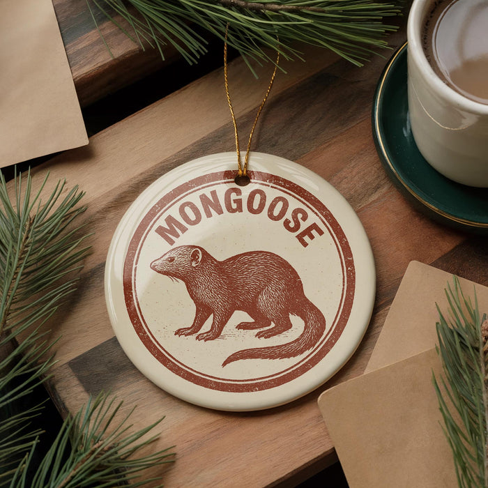 A circular ornament featuring a brown mongoose is displayed on a wooden surface, surrounded by pine branches and a cup of coffee.