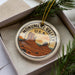 A decorative ornament in a box, featuring a circular design with a desert landscape and mountains, along with the text "MONUMENT VALLEY U.S.A."