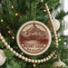 A Christmas tree decorated with ornaments, including a circular ornament with a mountain and lake design, and a string of wooden beads.