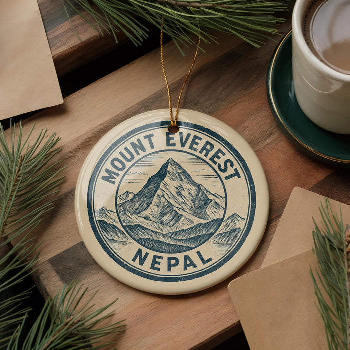 A circular ornament with the text "Mount Everest Nepal" on it, surrounded by pine branches and a cup of coffee on a wooden surface.