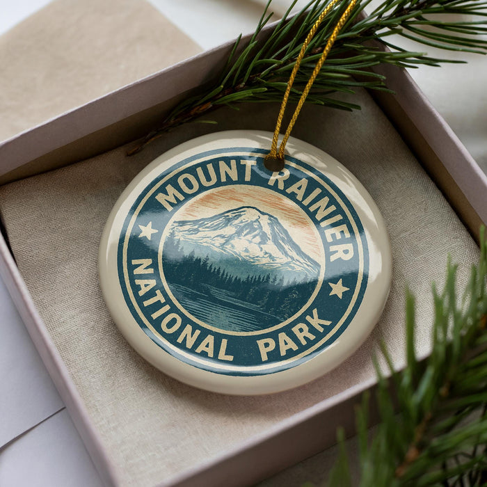 A round ornament with the text "MOUNTAIN RAINIER NATIONAL PARK" printed on it, surrounded by pine branches.