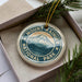 A round ornament with the text "MOUNTAIN RAINIER NATIONAL PARK" printed on it, surrounded by pine branches.
