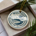 A circular ornament with the text "MUSTIQUE SAINT VINCENT AND THE GRENADAINES" printed on it, surrounded by pine branches.