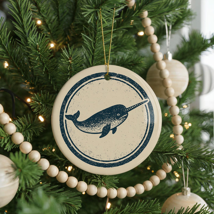 A Christmas tree decorated with ornaments, including a circular ornament featuring a blue and white image of a narwhal.