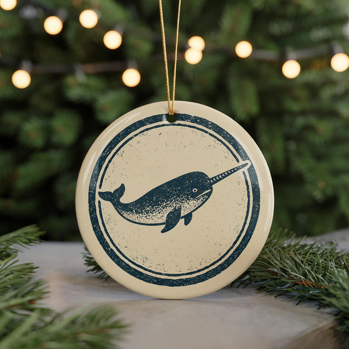 A circular ornament featuring a graphic of a narwhal is displayed against a blurred background of a Christmas tree with twinkling lights.