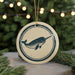 A circular ornament featuring a graphic of a narwhal is displayed against a blurred background of a Christmas tree with twinkling lights.