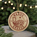 A circular ornament with the text "NAXOS GREECE" and an illustration of a Greek island, surrounded by Christmas lights and greenery.