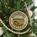 A circular ornament on a Christmas tree, featuring the text "NGORONGOORO TANZANIA" and an illustration of a landscape with mountains and a lake.