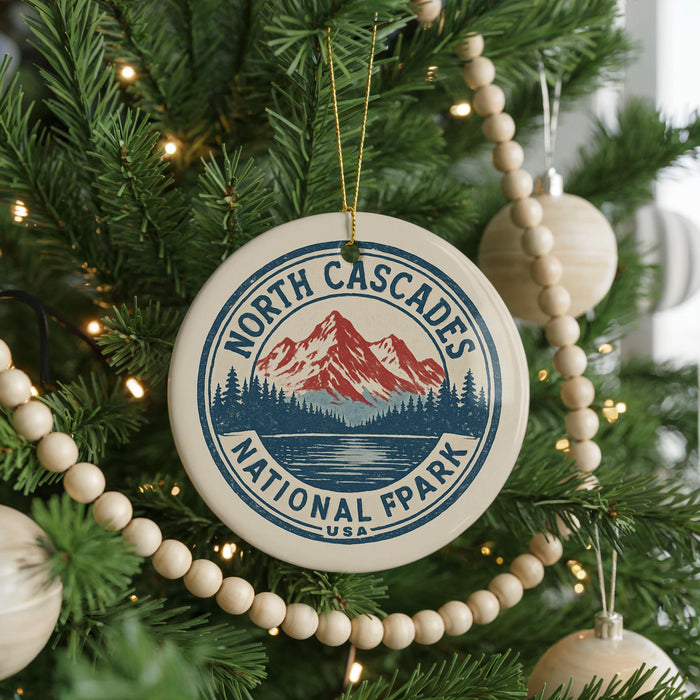 A Christmas tree decorated with ornaments, including a circular ornament with a mountain and lake design, surrounded by lights and greenery.
