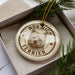 A decorative ornament featuring a terrier dog's head, with the text "NORwich Terrier" printed on it, placed inside a box surrounded by pine branches.