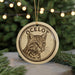A circular ornament featuring a close-up of a cat's face, with the word "OCELOT" written around the edge.