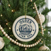 A Christmas tree decorated with ornaments, including a circular ornament with a graphic of a city and mountains, and a beaded ornament.