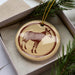 A ceramic ornament in the shape of a zebra is displayed in a box, surrounded by pine branches.