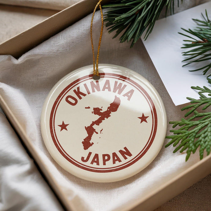 A circular ornament with the text "OKINAWA JAPAN" printed on it, surrounded by pine branches and a white paper.