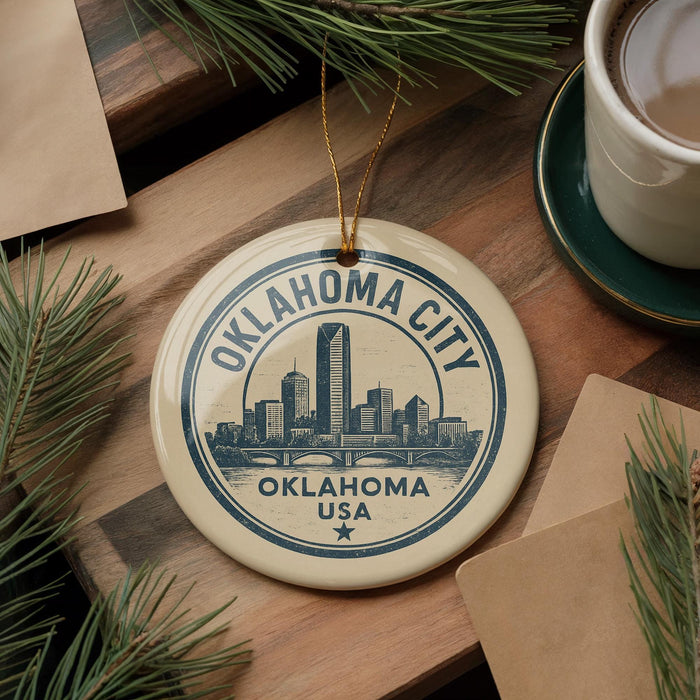 A circular ornament with the text "OKLAHOMA CITY USA" and a graphic of a city skyline is displayed on a wooden surface, surrounded by pine branches and a cup of coffee.