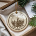 A circular ornament with the text "OLD TOWN TALLINN" and "ESTONIA" printed on it, hanging from a string. The ornament is placed on a white surface, with some greenery visible in the background.