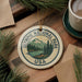 A circular ornament with the text "OLYMPIC NATIONAL PARK USA" and a mountain landscape design, hanging on a wooden surface.