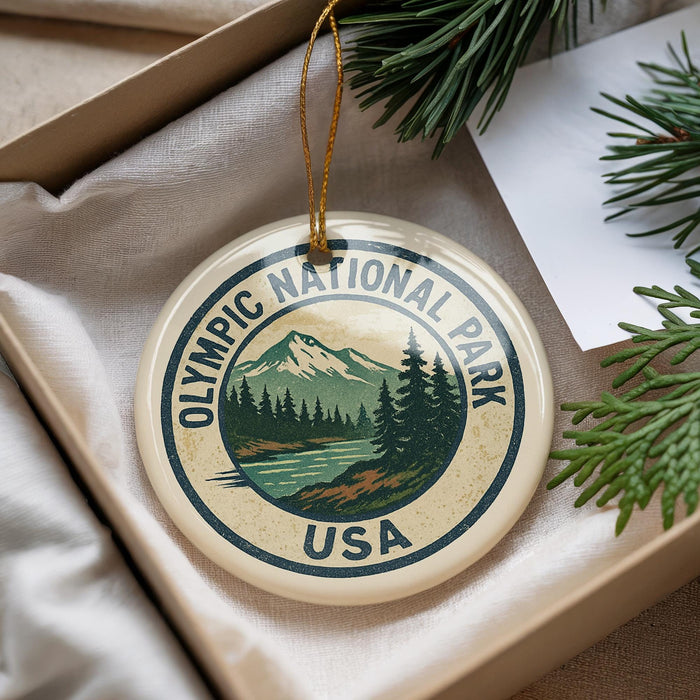A round ornament with the text "OLYMPIC NATIONAL PARK USA" and a mountain landscape design, hanging from a string.