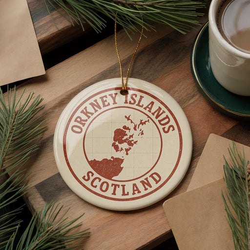 A circular ornament with the text "ORKNEY ISLANDS SCOTLAND" and a map of the islands, placed on a wooden surface with pine branches and a cup of coffee nearby.