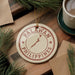 A circular ornament with the text "PALAWAN PHILIPPINES" and a map of the Philippines, placed on a wooden surface next to a cup of coffee and some pine branches.