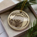 A circular ornament with a cat image and the text "PALLAS'S CAT" printed on it, placed inside a box with pine branches.