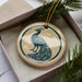 A decorative ornament in a box, featuring a blue and white design of a peacock.