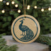 A round ornament featuring a blue peacock design is displayed against a blurred background of a Christmas tree with twinkling lights.